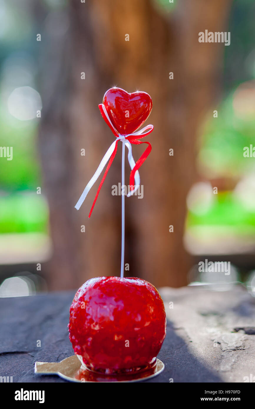 Manzana de caramelo con un mango y un corazón rojo en la parte superior Foto de stock