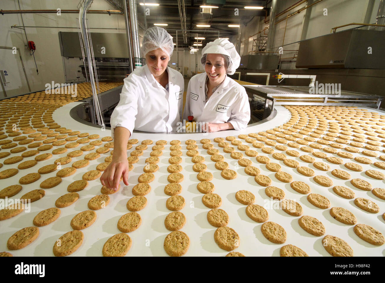 Línea de producción con galletas y obreros de fábrica Foto de stock