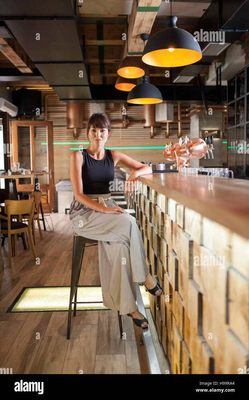Mujer con pelo marrón sentado en el mostrador de bar en la cafetería. Foto de stock