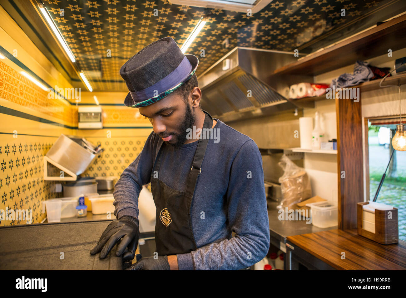 Hombre con sombrero y delantal trabajando en cocina comercial de camión de alimentos Foto de stock