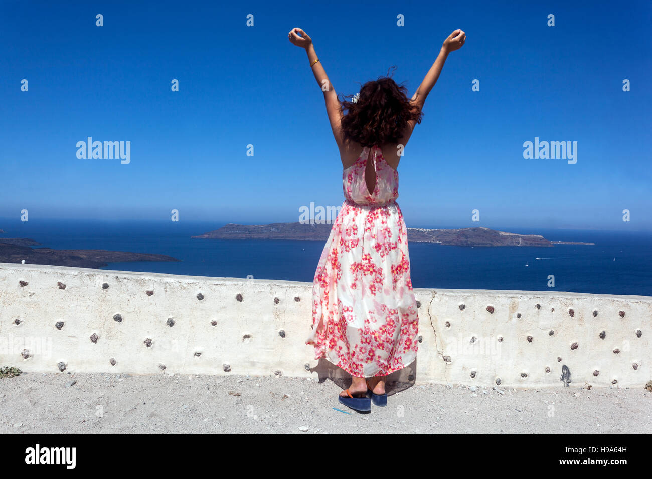 Una mujer de pie en una terraza sobre el mar con las manos elevadas y disfruta de la sensación de la brisa, Santorini turística Grecia atmósfera Foto de stock
