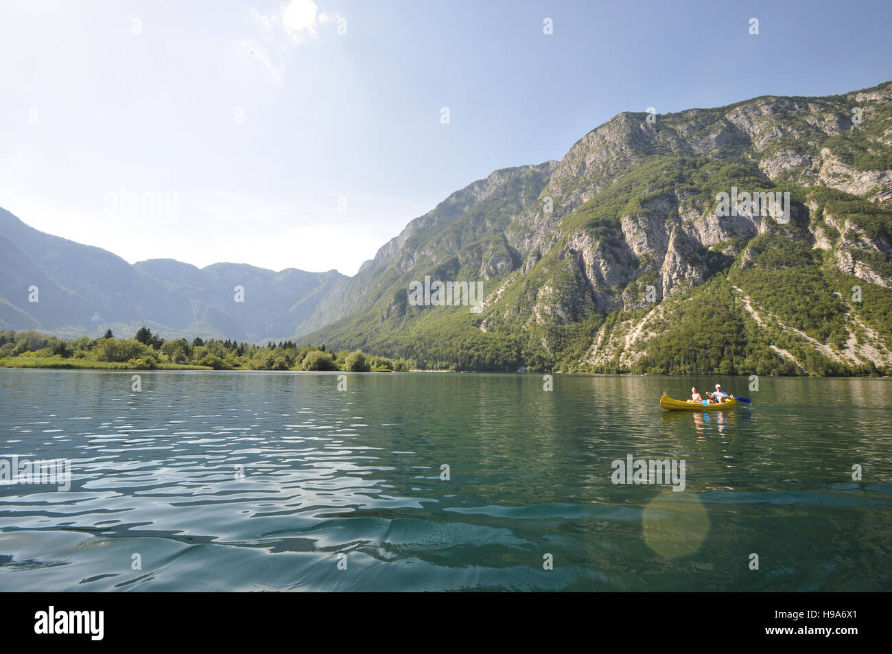 Dos personas en un kayak amarillo en el lago Bohinj, Eslovenia, con acantilados de las montañas de los Alpes Julianos en el fondo Foto de stock