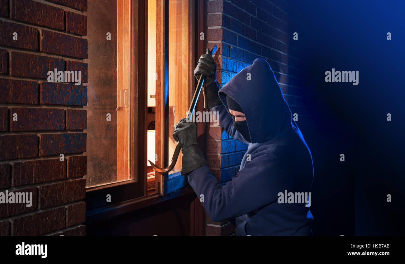 Ladrón Con una palanqueta para irrumpir en una casa por la noche con la habitación a izquierda y derecha para tipo Foto de stock