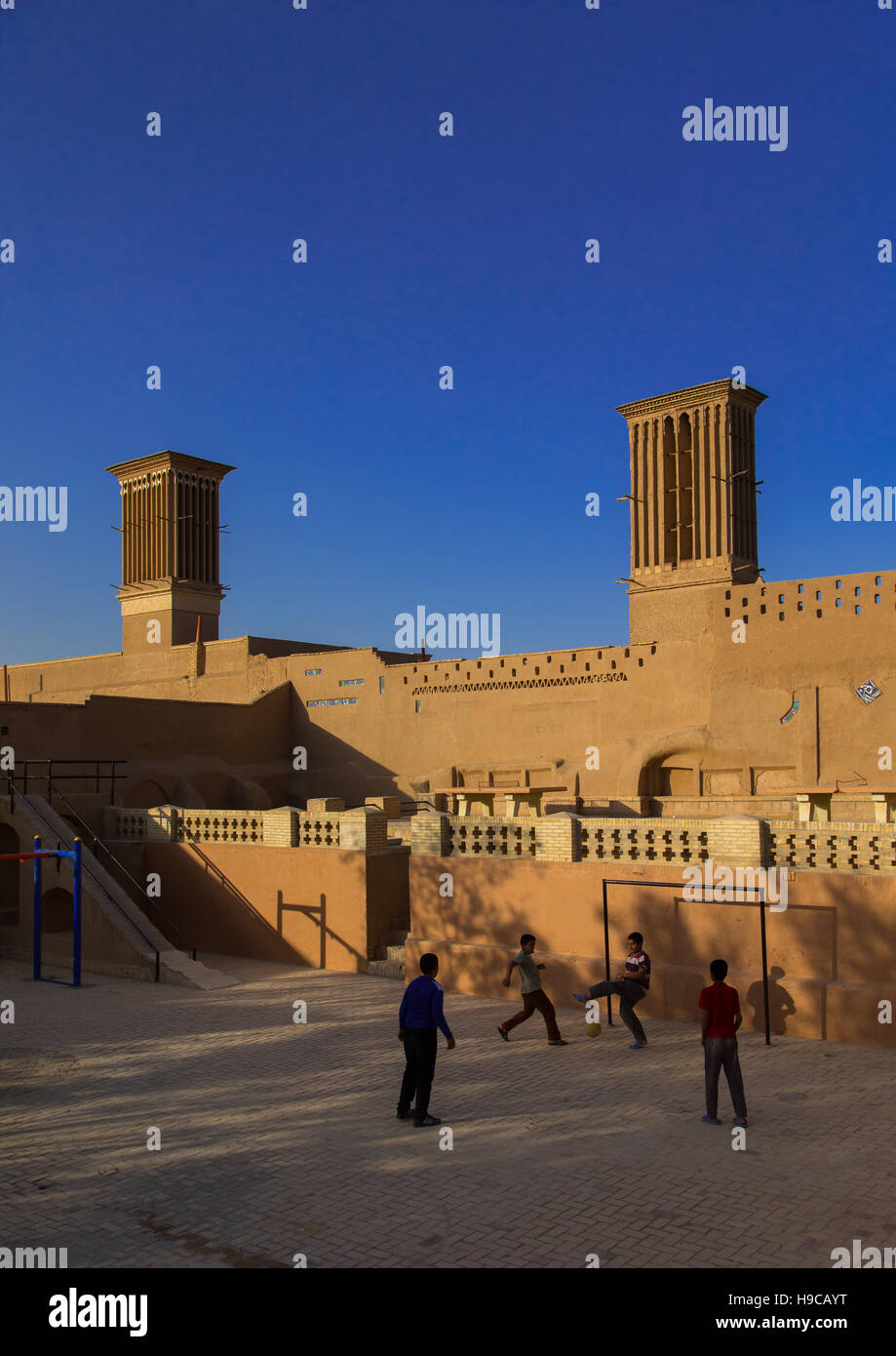 Niños jugando al fútbol delante de ind torres utilizadas como sistema de refrigeración natural en la arquitectura tradicional iraní, la provincia de Yazd, en Yazd, Irán Foto de stock