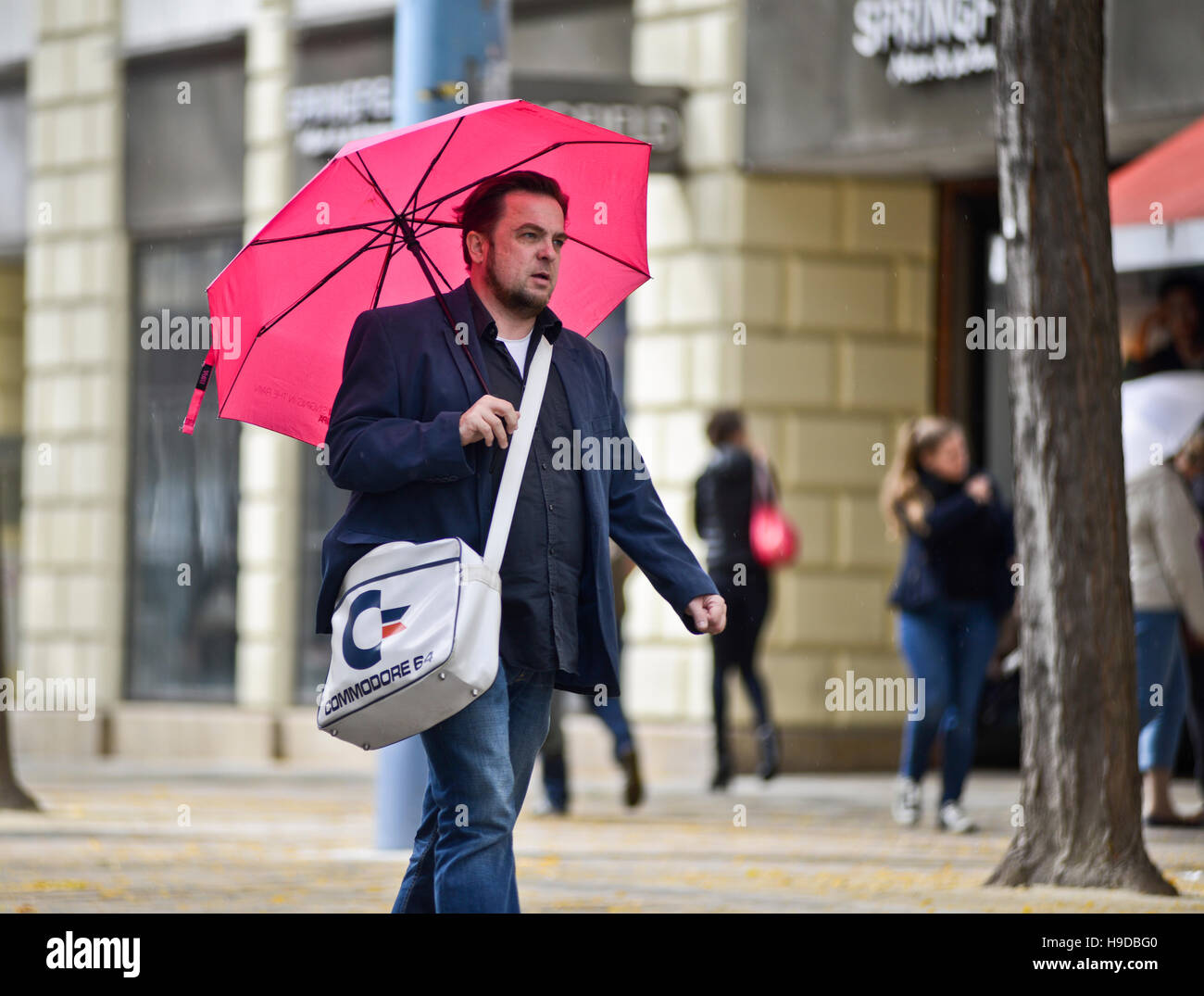 Hombre caminando por la calle vistiendo un paraguas rosa y bolsa de la marca  Commodore. Viena, Austria Fotografía de stock - Alamy