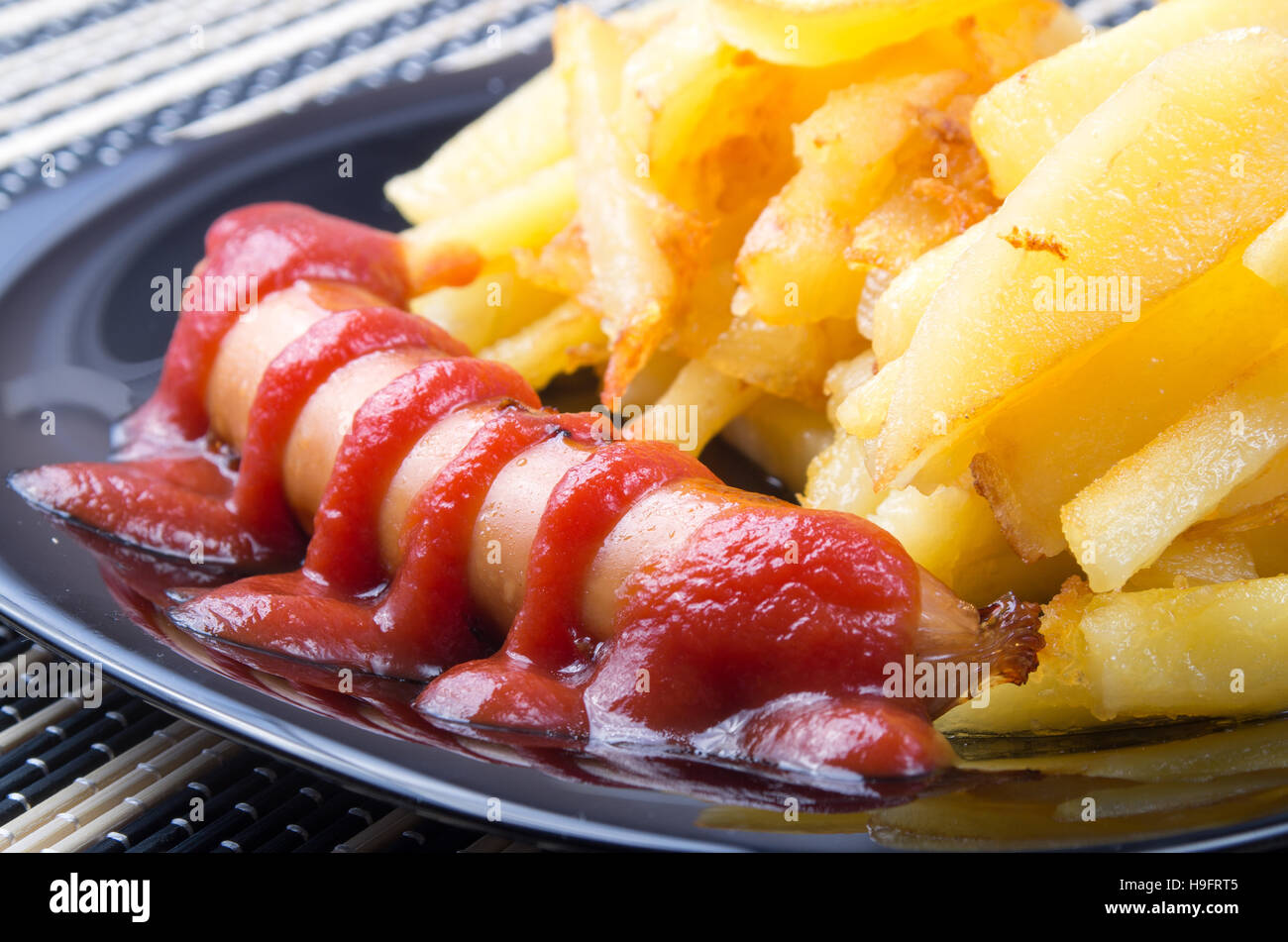 Detalle de una placa negra con salchichas a la parrilla con salsa de tomate y patatas fritas closeup Foto de stock