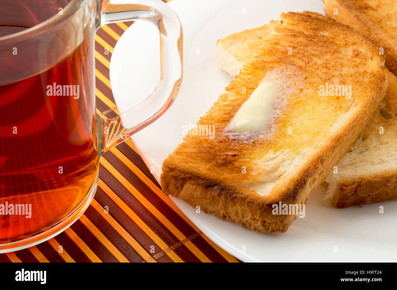 Taza de té y tostadas con mantequilla caliente sobre una placa blanca para desayunar cerrar Foto de stock