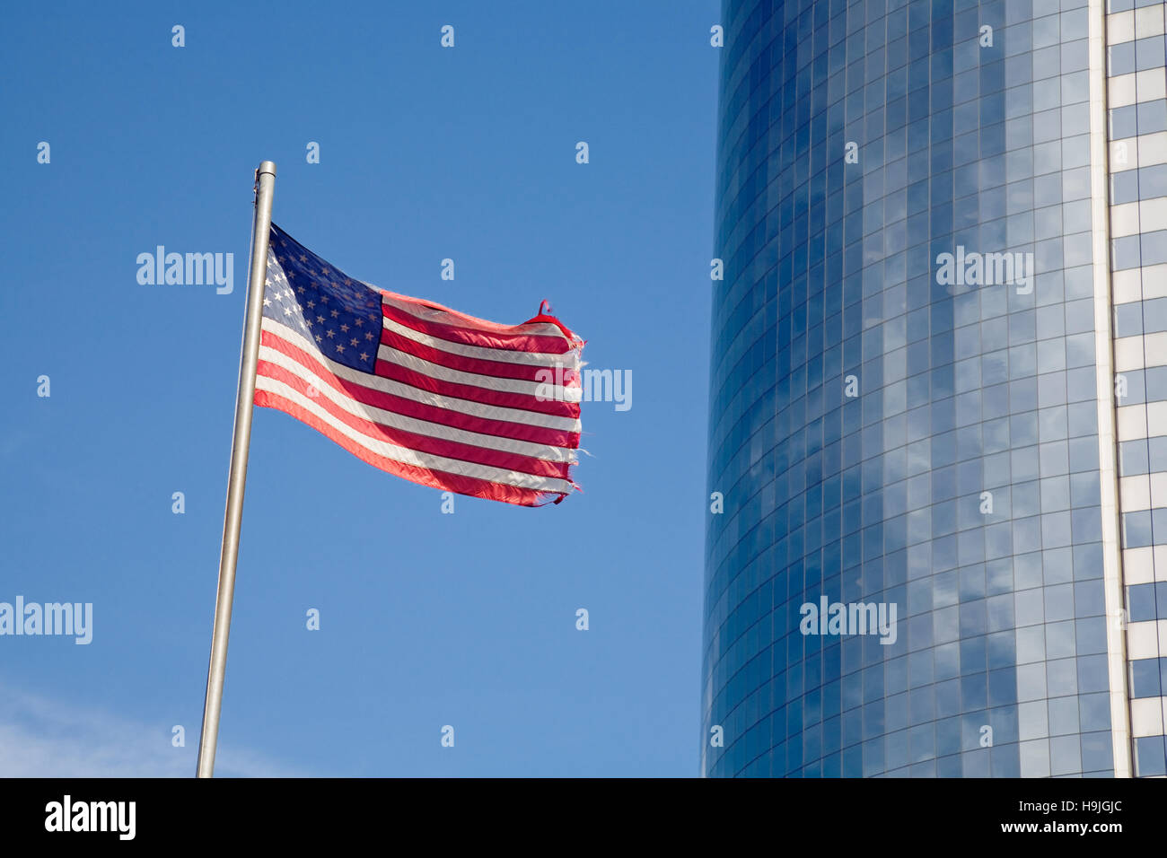 Ondea la bandera de las barras y estrellas junto a un rascacielos moderno con fachada de cristal en el distrito financiero de Manhattan, en la Ciudad de Nueva York. El desenfoque de la ed Foto de stock