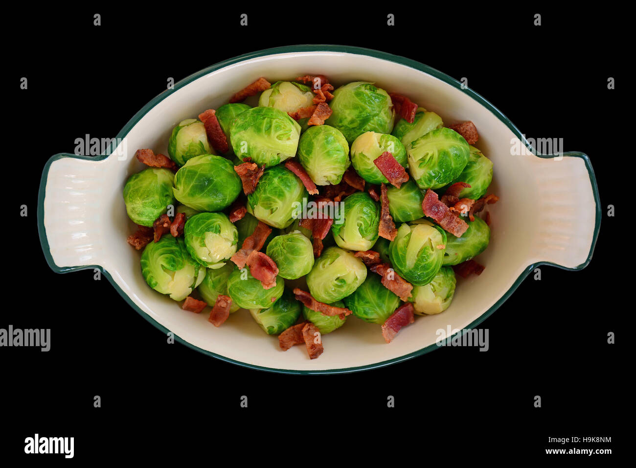 Las coles de bruselas frescas cocinadas al vapor con tocino crujiente bits en vintage plato aislado en negro. Rodada con luz natural desde la perspectiva aérea. Foto de stock