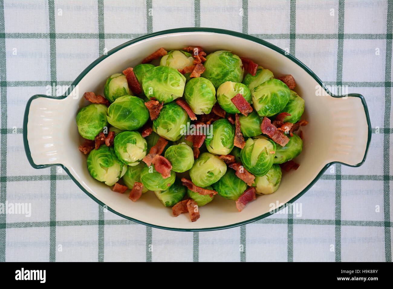 Las coles de bruselas frescas cocinadas al vapor con tocino crujiente bits en vintage plato de tela verde y blanco. Rodada en luz natural de sobrecarga perspectiv Foto de stock