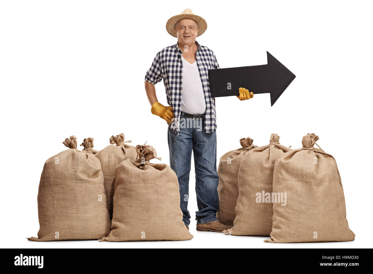 Longitud completa el retrato de un anciano agricultor de pie entre los sacos de arpillera y sosteniendo una flecha orientada hacia la derecha aislado sobre fondo blanco. Foto de stock