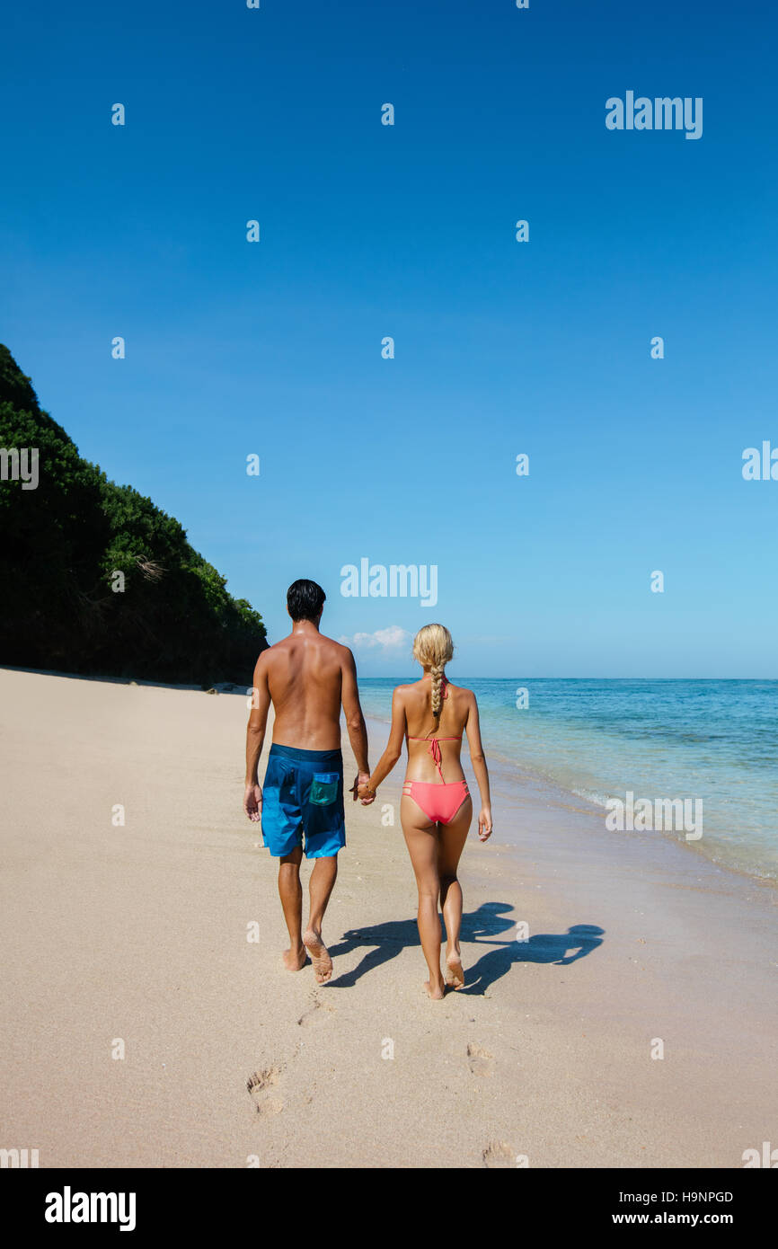 Vista trasera foto de luna de miel tomados de la mano caminando por la orilla del mar. Pareja en amor, relajarse en vacaciones de verano en la playa. Foto de stock