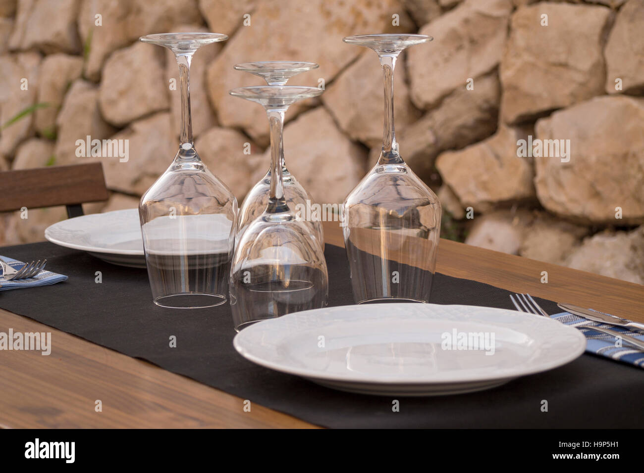 Mesa con platos y copas de vino blanco al revés, con fondo de piedra  Fotografía de stock - Alamy