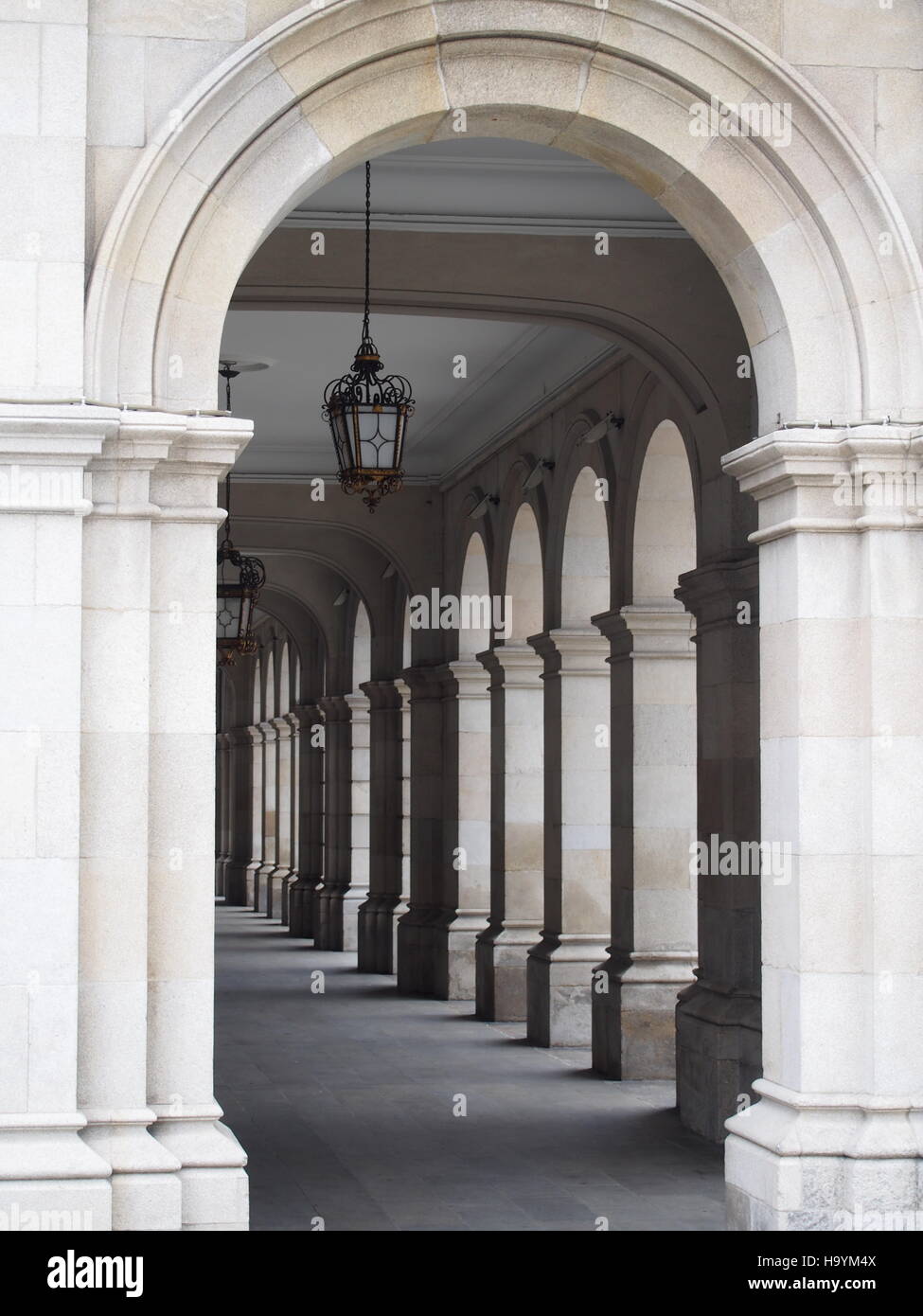 Pasarela arqueada, galería claustro o columnata en la parte delantera del Ayuntamiento de La Coruña, Galicia, España, con pilares, arcos y lámpara colgante o linternas Foto de stock