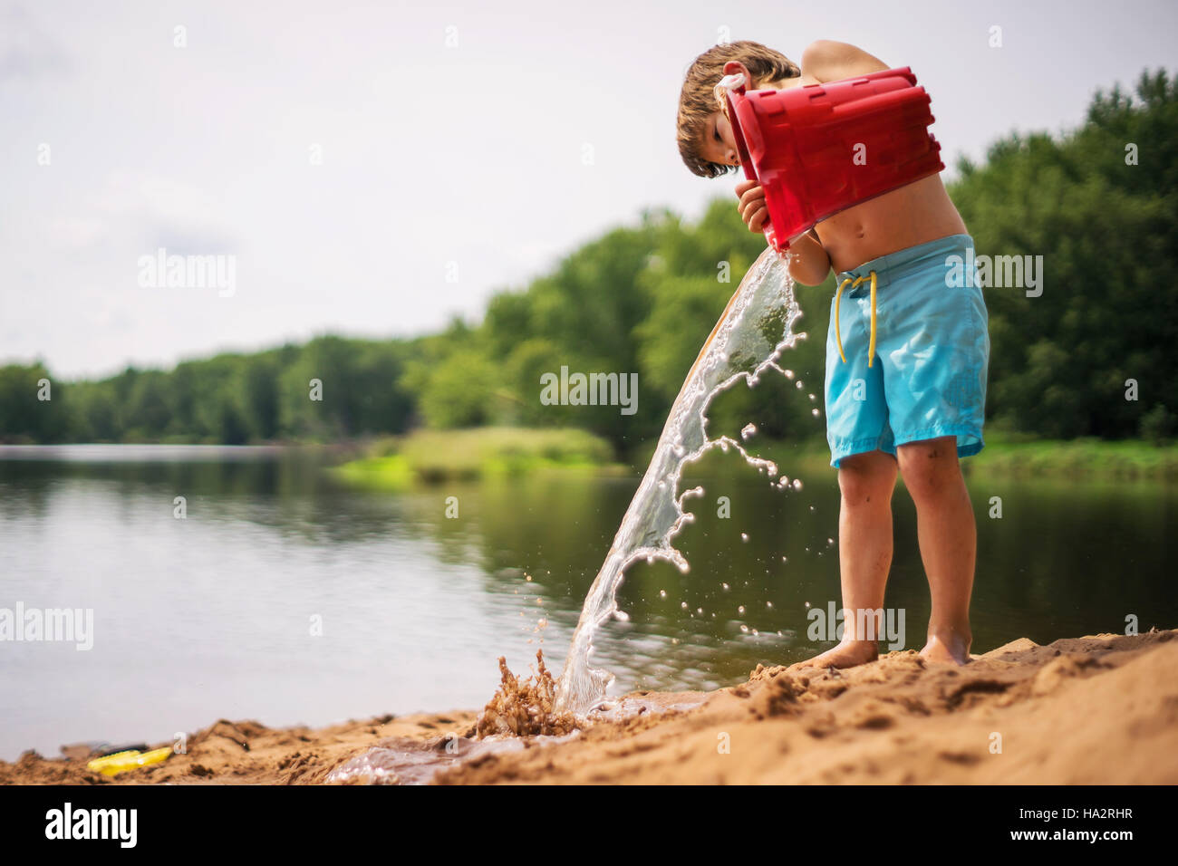 Boy vaciando un balde de agua en la playa Foto de stock