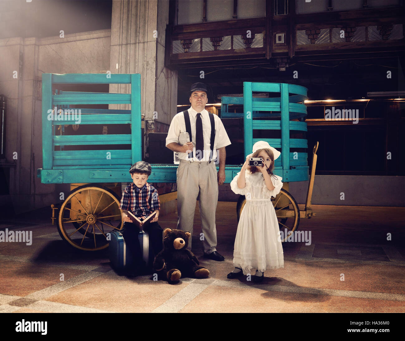Una antigua familia vintage está esperando en una vieja estación de tren por un carrito de equipaje para el concepto de viaje o de vacaciones. Foto de stock