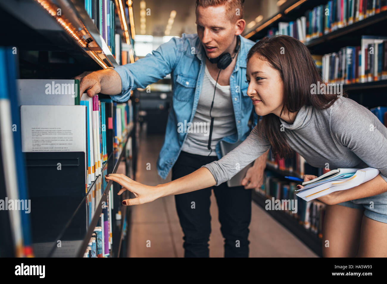 Los jóvenes estudiantes encontrar libros de referencia en la biblioteca de la universidad. El hombre y la mujer en la búsqueda de información para sus estudios. Foto de stock