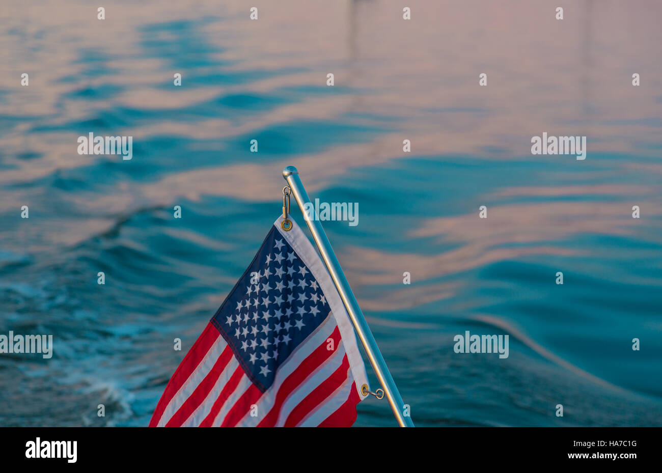 Imagen de detalle de una bandera americana en un poste de acero inoxidable con agua salada en segundo plano. Foto de stock
