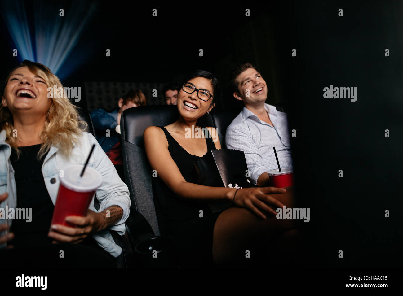 Mujer sonriente viendo la película con sus amigos en la sala de cine. Grupo de personas en la sala de cine viendo la película de comedia. Foto de stock