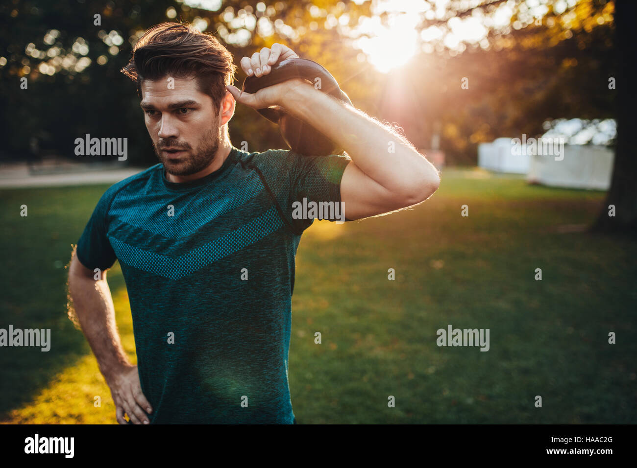 Retrato de hombre joven fuerte ejerciendo con kettlebell. Colocar y musculoso hombre entrenamiento en parque en la mañana. Foto de stock