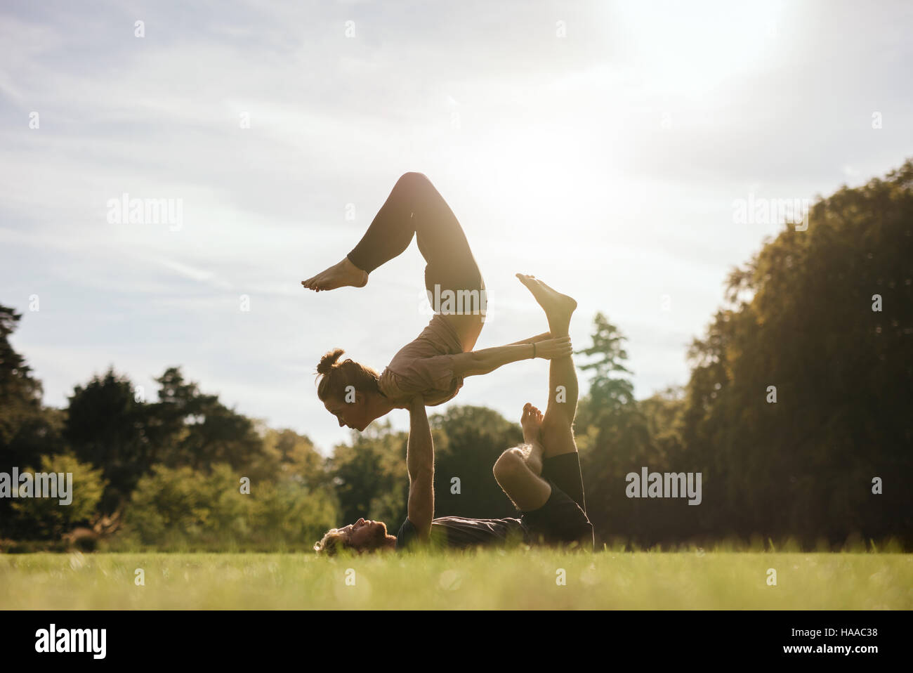 Pareja joven y saludable hacer acro yoga al aire libre. El hombre y la mujer haciendo varias posturas de yoga par en el parque. Foto de stock