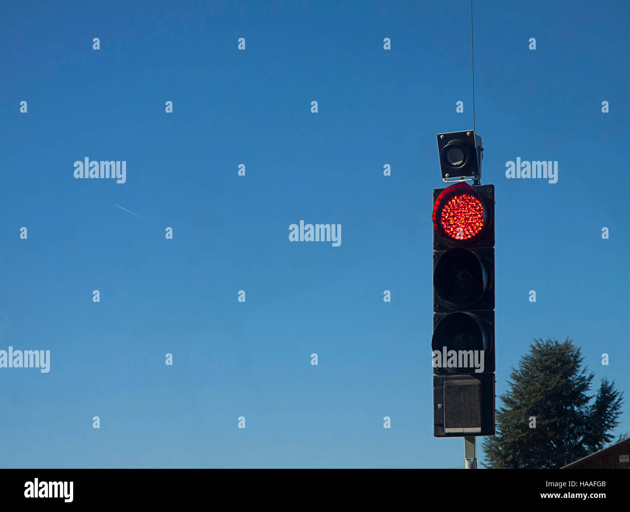 Semáforo con luz roja encendida para regular el tráfico en el cruce del camino, fondo de cielo azul Foto de stock