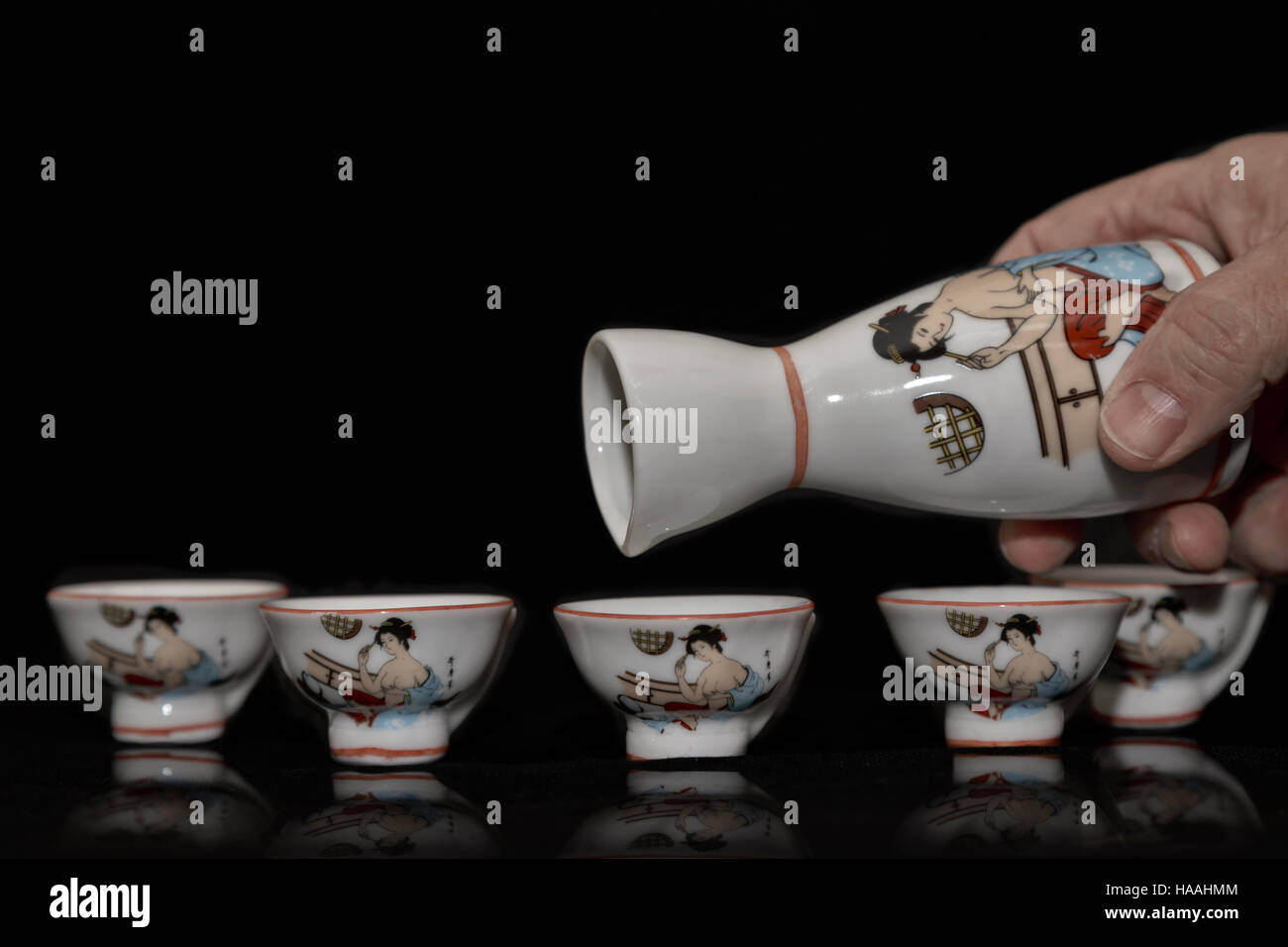 Echando mano de un minúsculo antigüedades asiáticas china jarra en una fila de vasos pequeños coincidentes sobre un fondo oscuro con espacio de copia Foto de stock