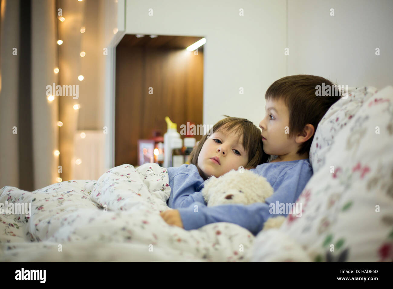 Dos lindos hijos, niños enfermos, permanecer en cama con fiebre, jugando con osito de peluche Foto de stock