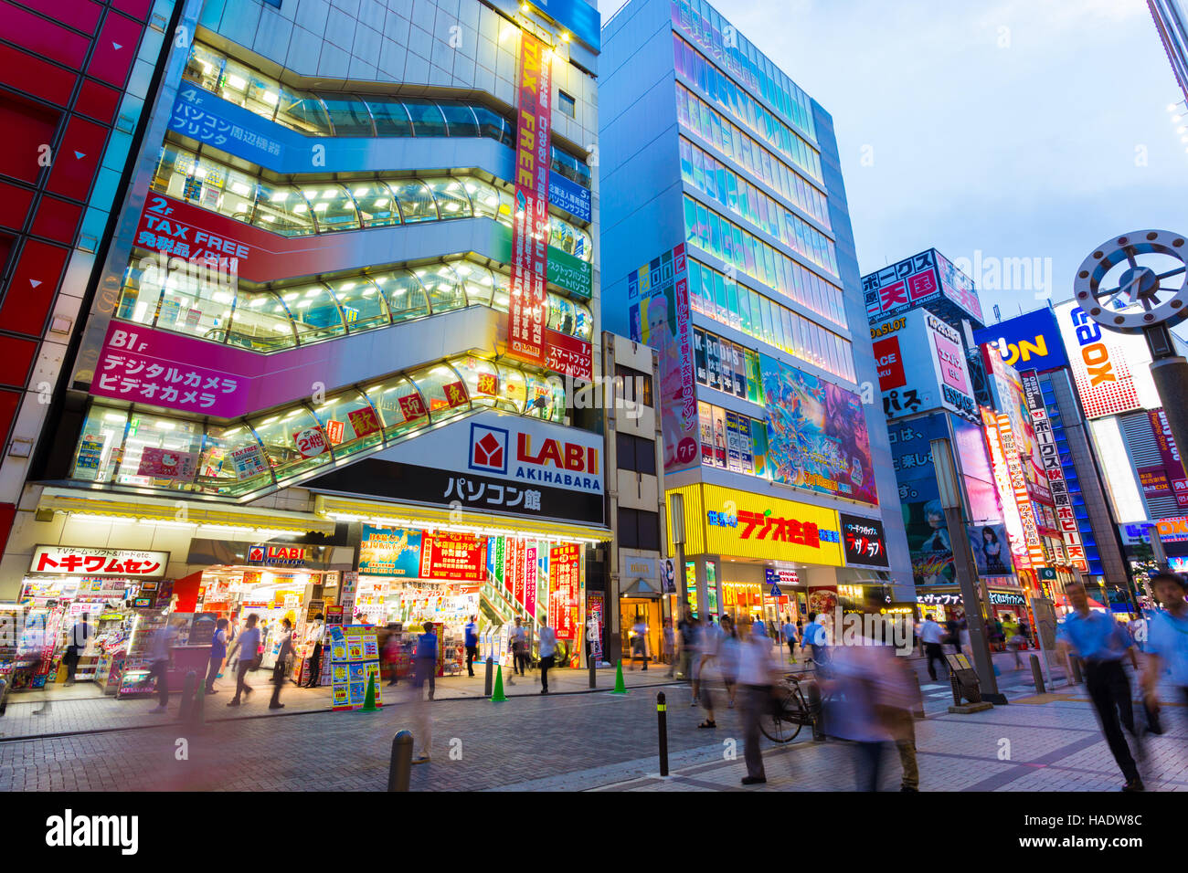 Multitudes de personas caminando, bullicioso barrio de cubo de electrónica Akihabara entre luces brillantes y letreros de tienda, advertis Foto de stock