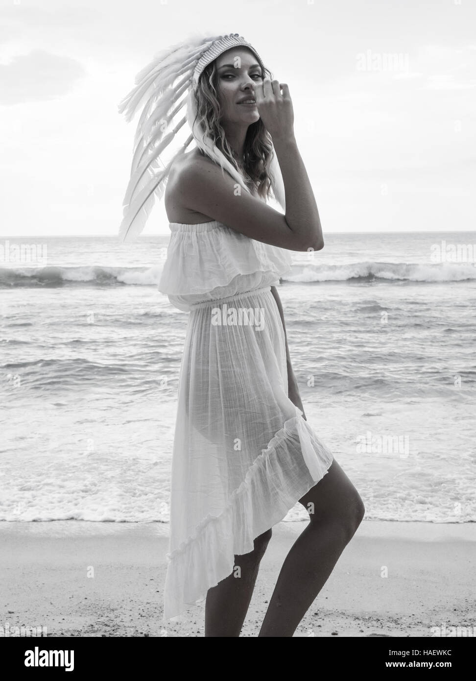 Mujer rubia vestidos de blanco y sombrero de plumas indio vestido blanco  mirando a la cámara y sonriendo mientras está de pie en la playa más  hermosa del mar y del cielo