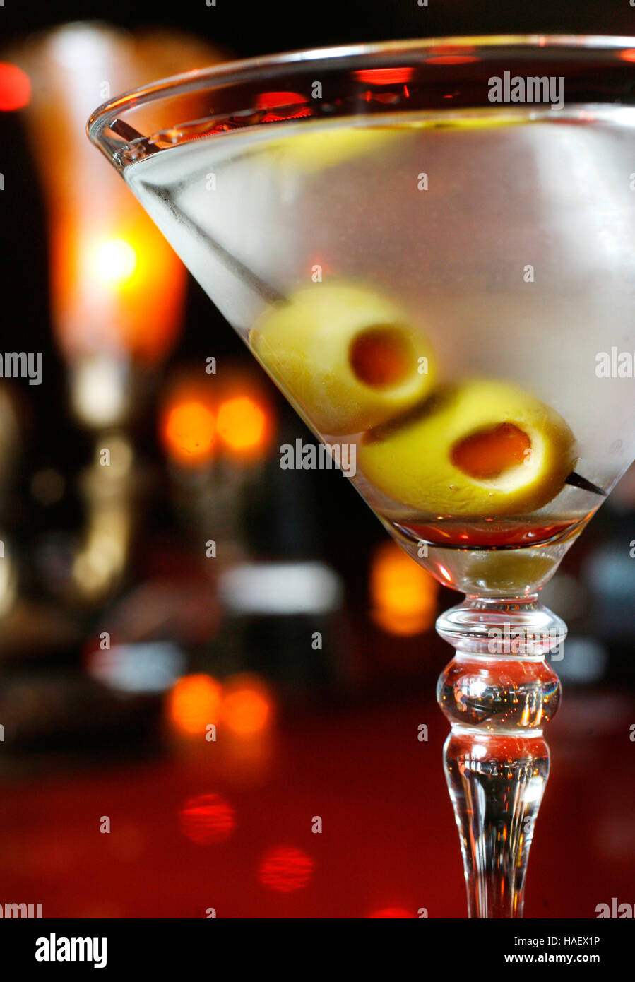 Un martini con aceitunas se sienta en un bar con un salón de cócteles. Foto de stock