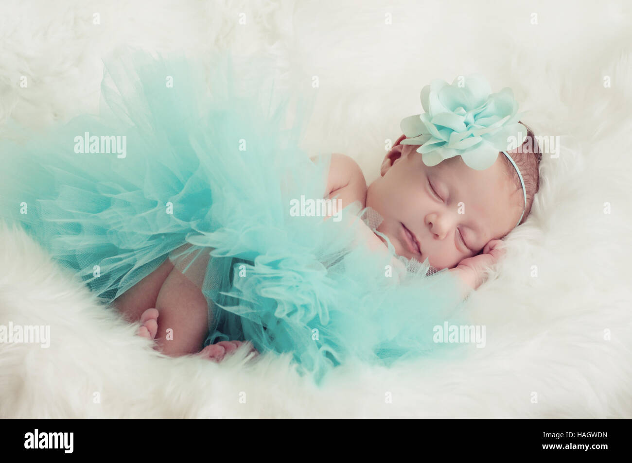 Precioso bebé niña en traje verde azulado poniendo en piel blanca. Foto de stock