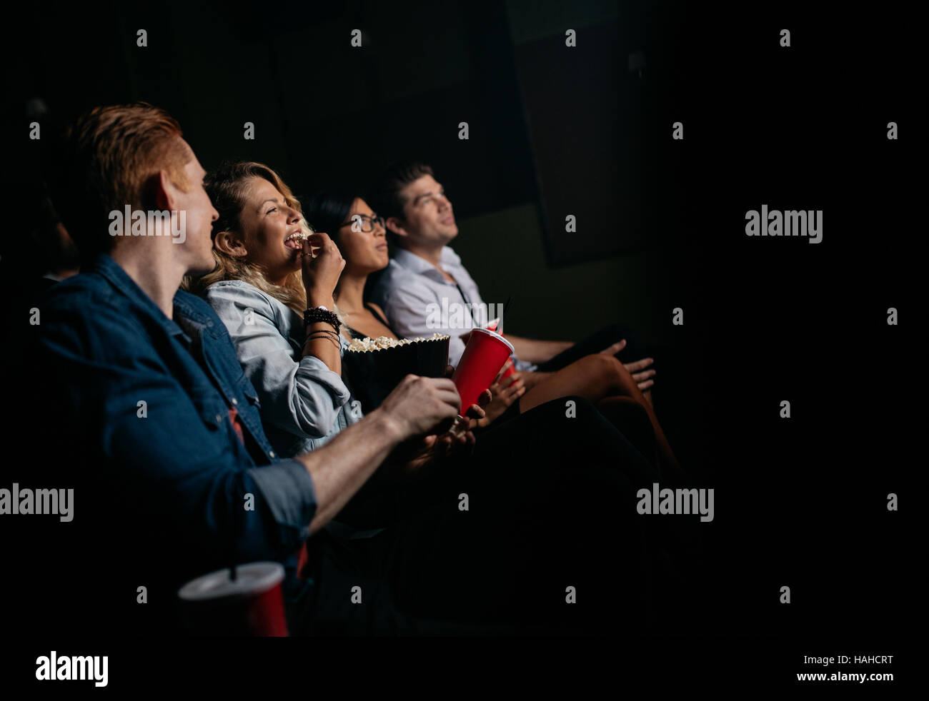 Grupo de jóvenes viendo la película en el cine. Amigos sentado en el cine con palomitas y refrescos. Foto de stock