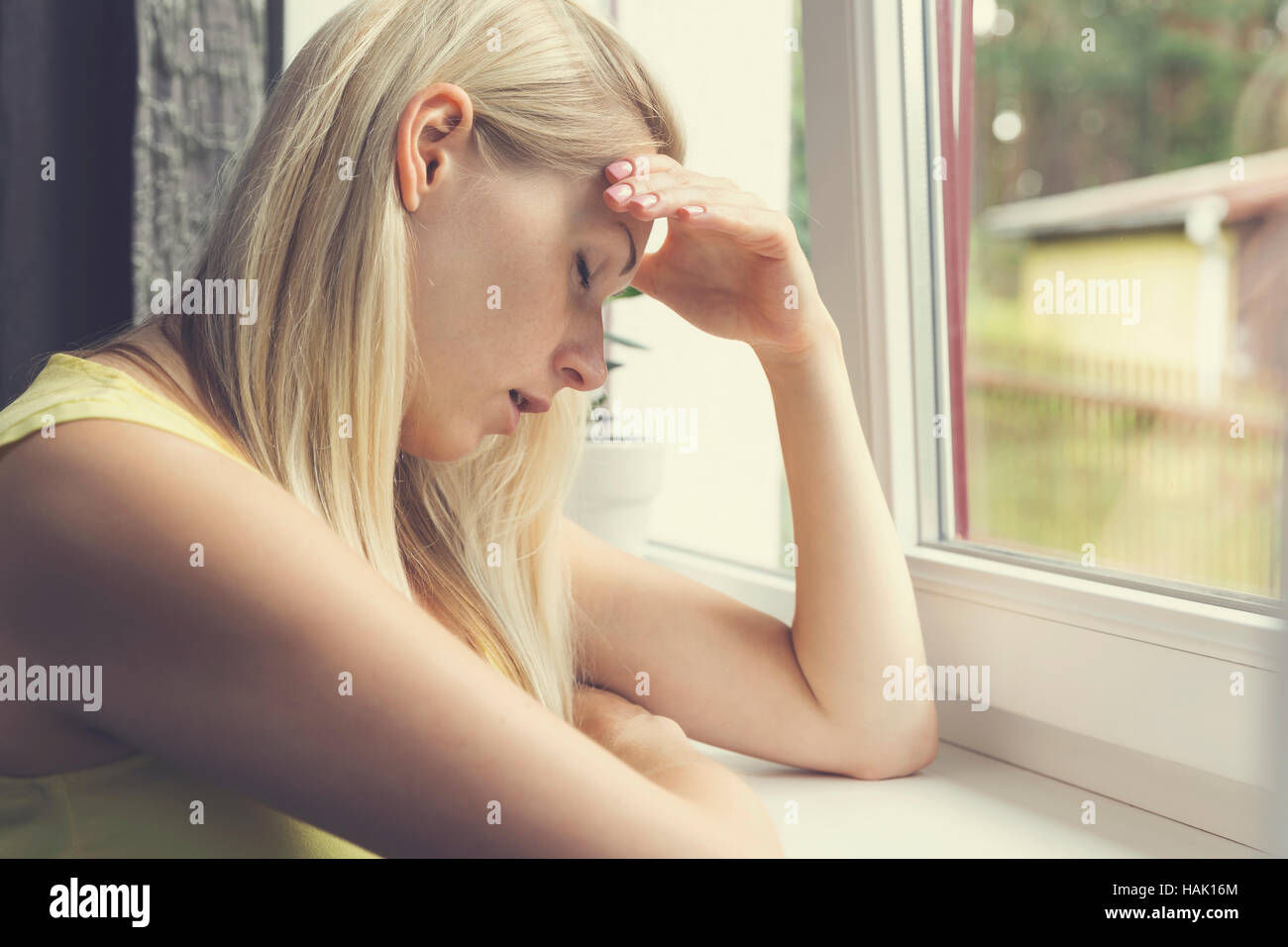 Cansado, deprimido mujer sentada por la ventana Foto de stock