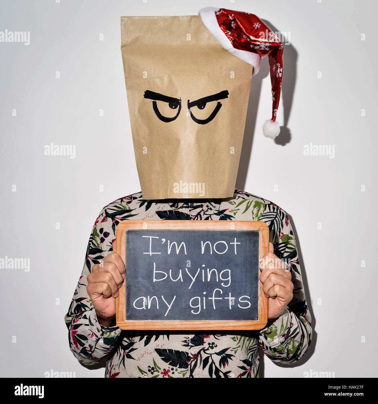 Un hombre joven vistiendo ropa casual con una bolsa de papel en la cabeza y un gorro de Papá Noel en la parte superior muestra una pizarra con el texto no estoy comprando regalos wr Foto de stock