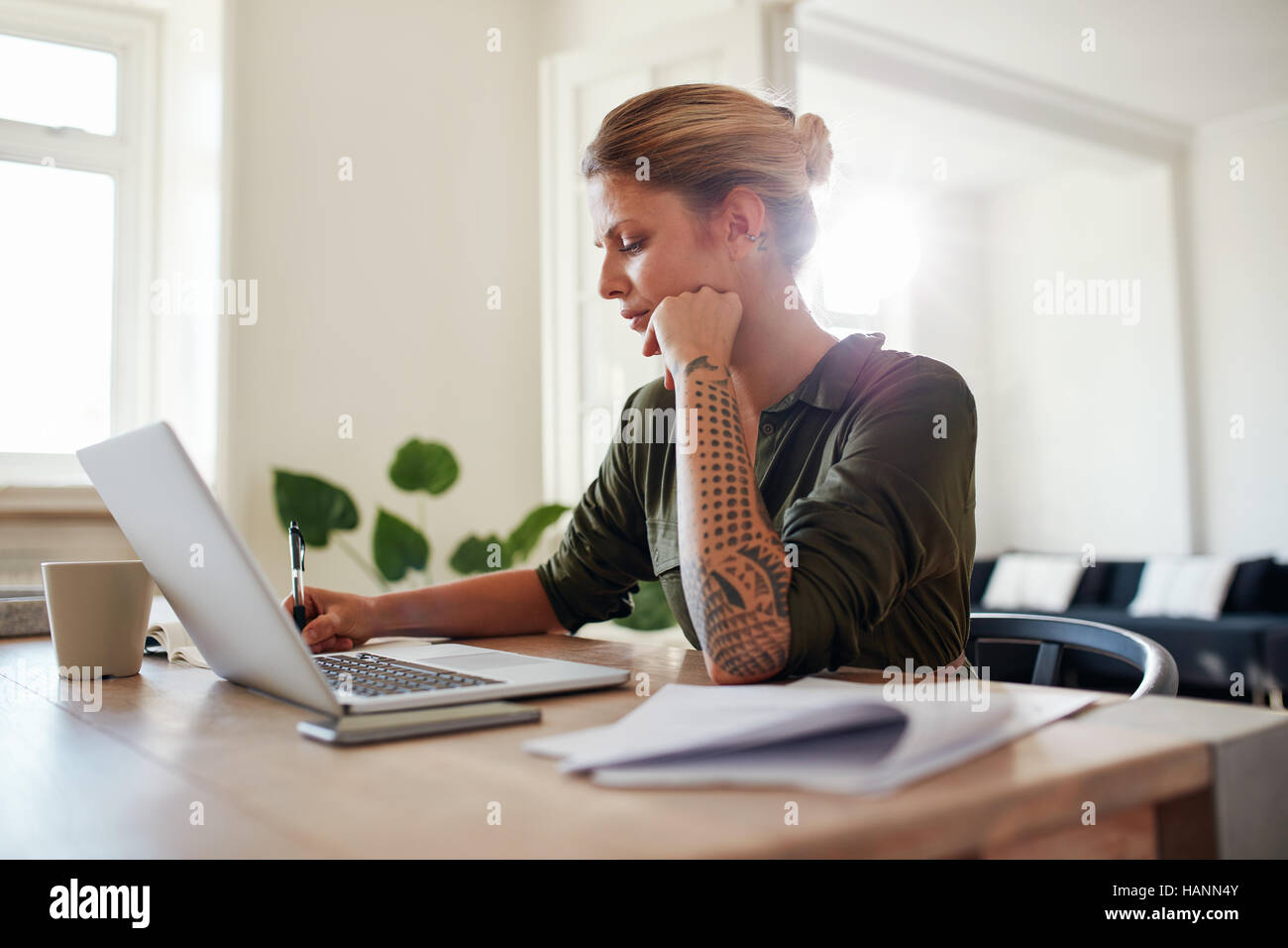 Foto de joven que trabaja en la oficina principal. Hermosa mujer sentada en la mesa con el ordenador portátil y documentos. Foto de stock
