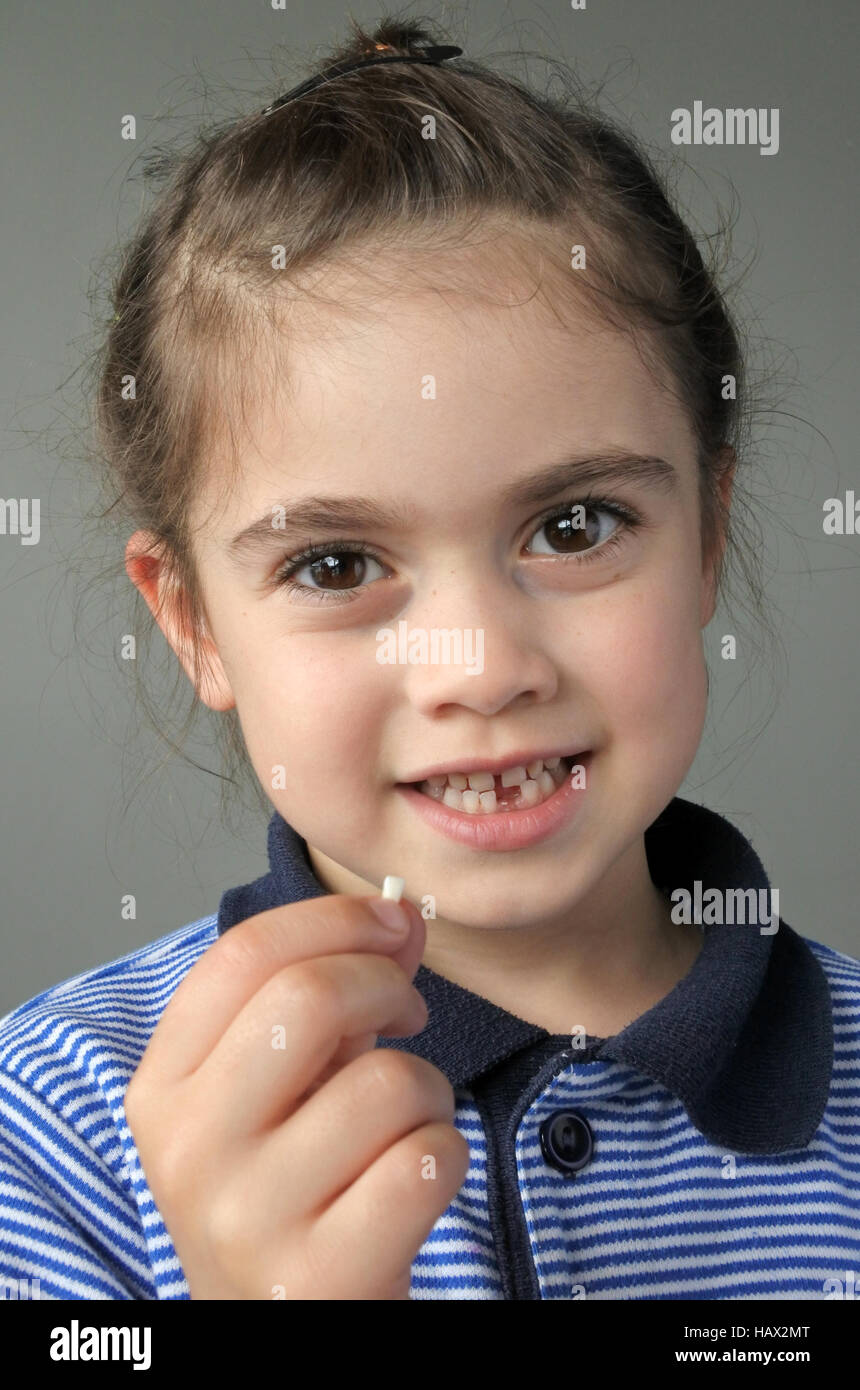 Feliz joven (6 años) mantiene su primera caída de dientes de leche, mira a la cámara. Concepto de salud en la infancia. La gente real espacio de copia Foto de stock