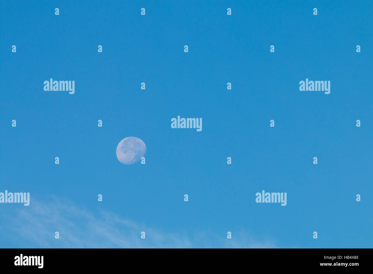 Luna en horario diurno. Débil pero vista detallada de la luna contra el cielo azul, ligera whisps de nube blanca debajo. Foto de stock