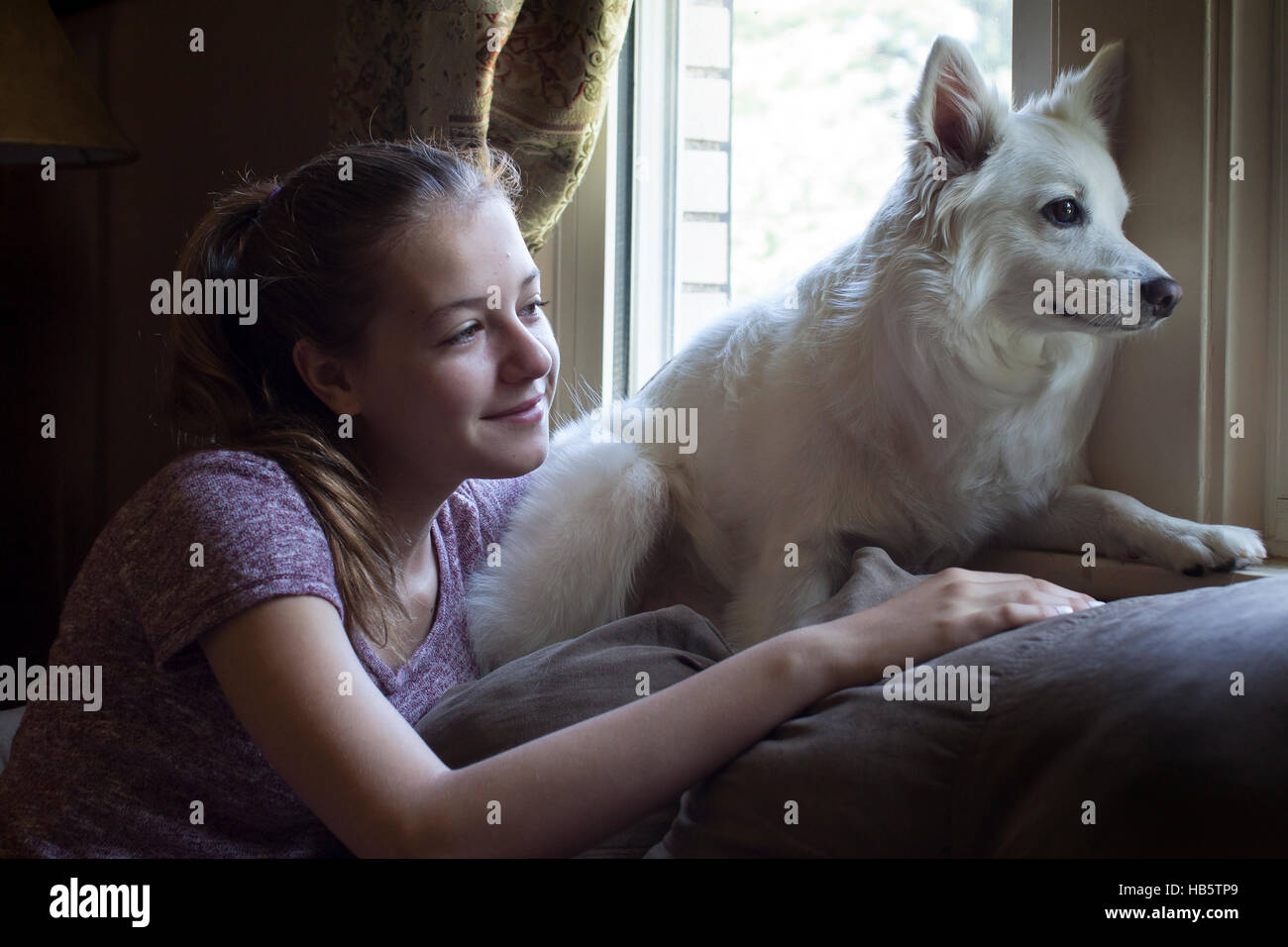 Teenage chica rubia con un perro blanco mirando a través de la ventana Foto de stock