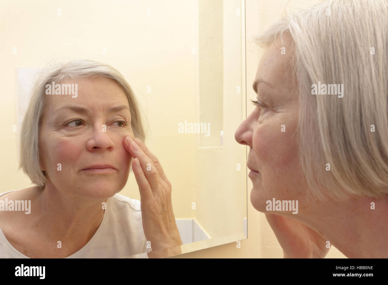 Concepto de envejecimiento, la tercera mujer tener un vistazo de cerca a las arrugas de su piel facial en un espejo, pensar en la cirugía estética Foto de stock