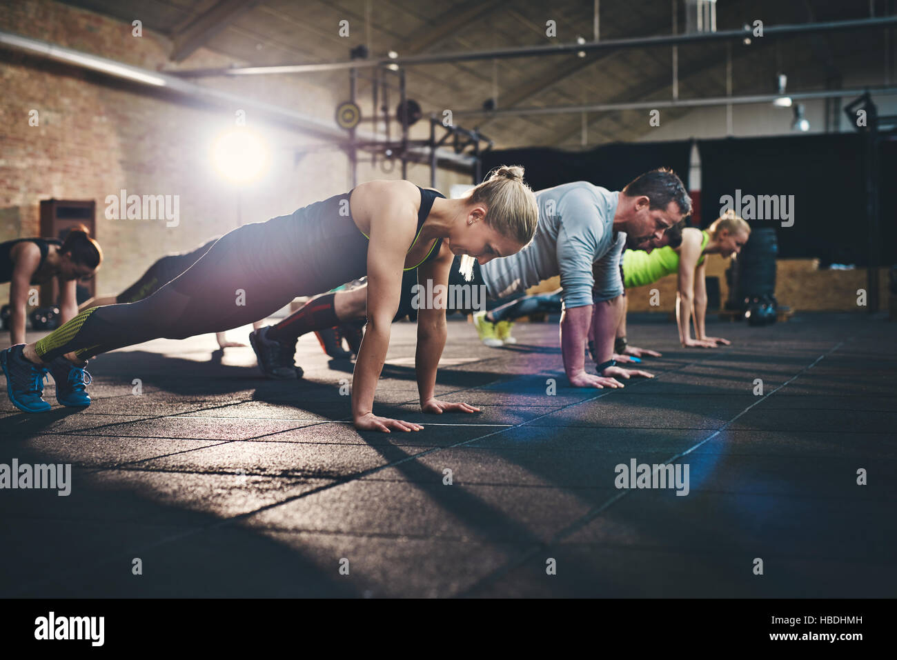 Grupo de adultos haciendo push up ejercicios físicos interiores cross-training fitness gimnasio con destellos de luz brillante sobre ellas. Foto de stock