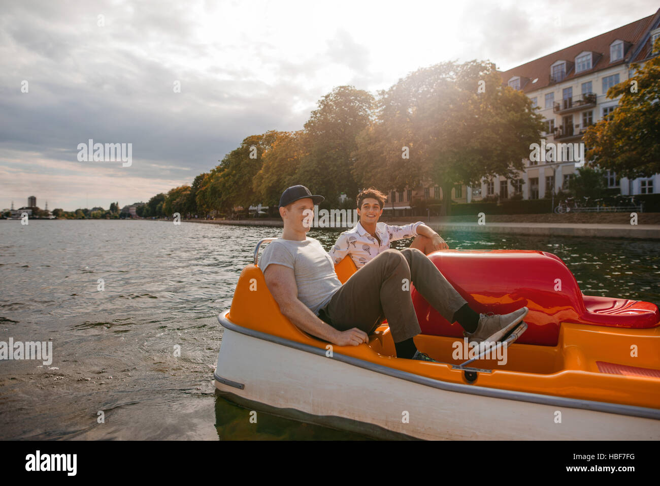 Tiro de dos jóvenes amigos sentado en bote a pedal y pedaleando. Los adolescentes varones el paseo en bote por el lago en la ciudad. Foto de stock