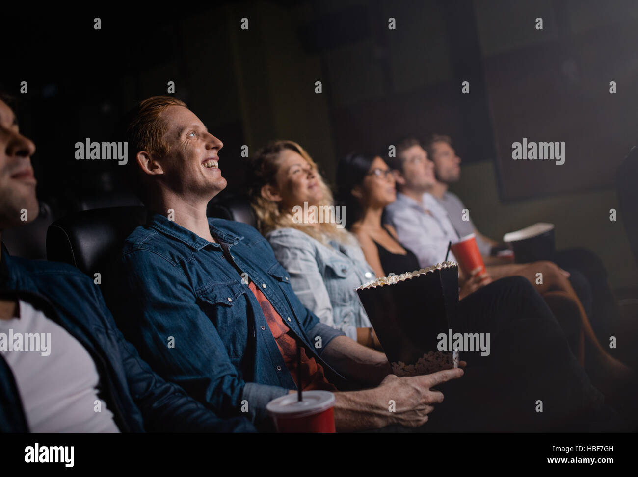 Grupo de gente sentada en el cine multiplex y viendo la película. Feliz jóvenes amigos viendo la película en el cine. Foto de stock