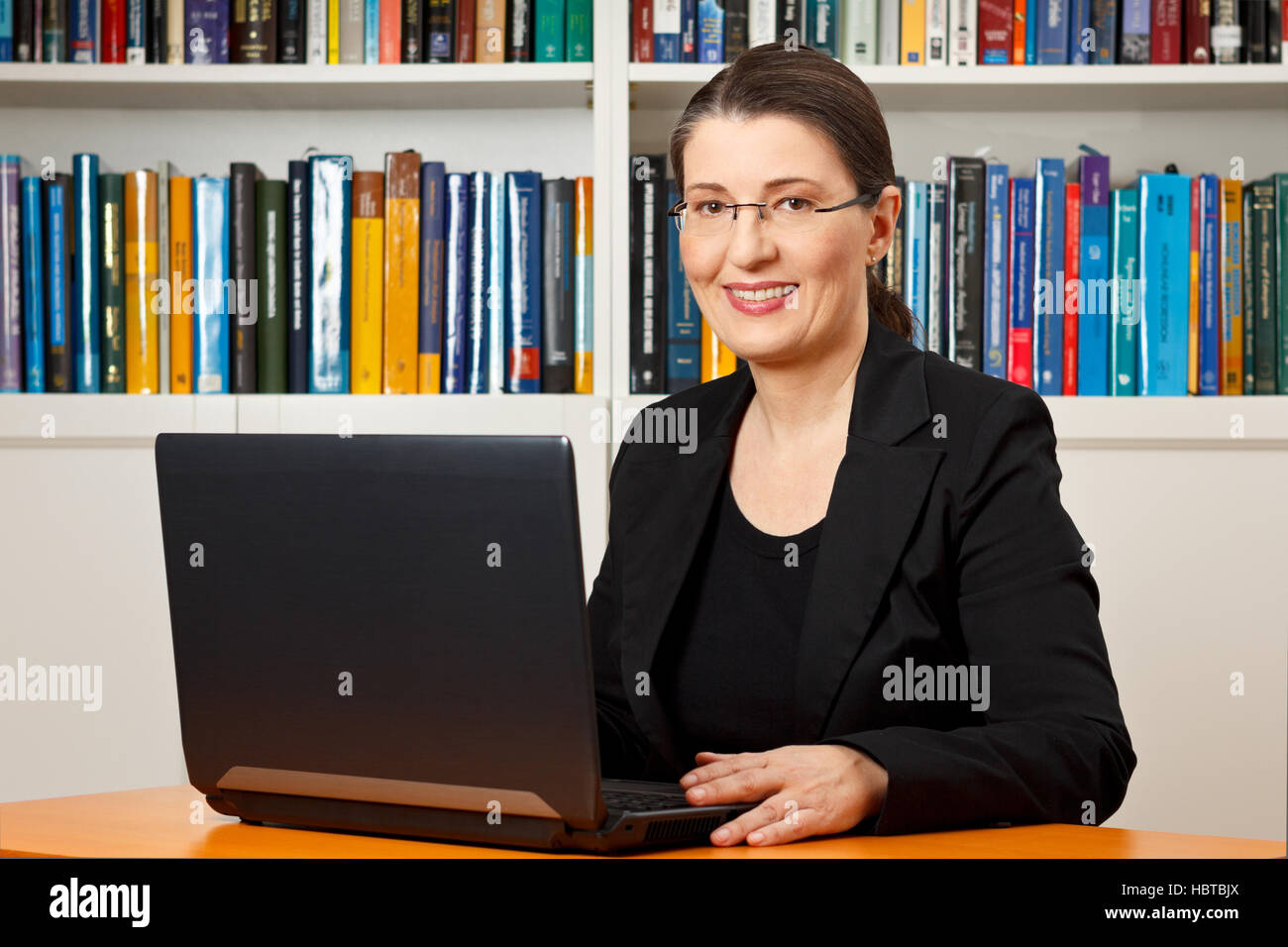 Amable mujer sonriente delante de su laptop en una biblioteca, maestro, tutor, profesor, consultor, consultoría Foto de stock