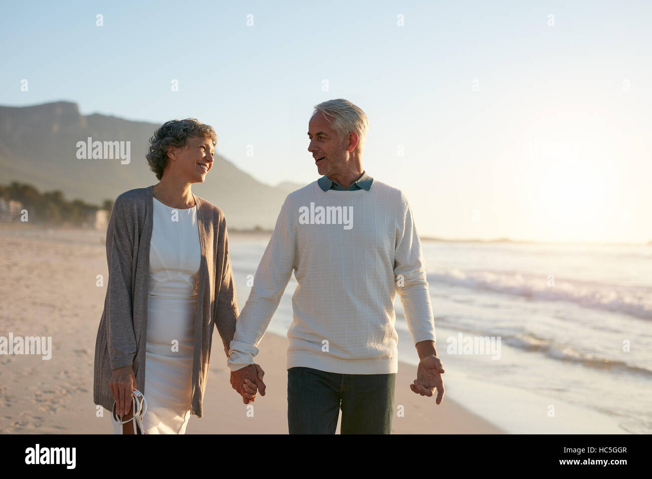 Retrato de romántica pareja senior caminando de la mano en la playa. Pareja amorosa un paseo a la orilla del mar. Foto de stock