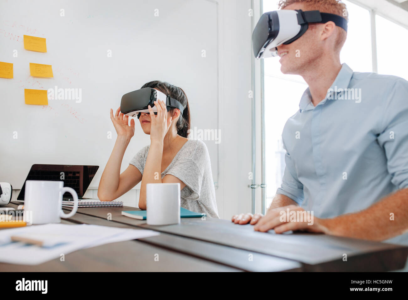 El hombre y la mujer joven sentada en una mesa y utilizando gafas de realidad virtual. Equipo empresarial con casco de realidad virtual en la oficina reunidos. Foto de stock