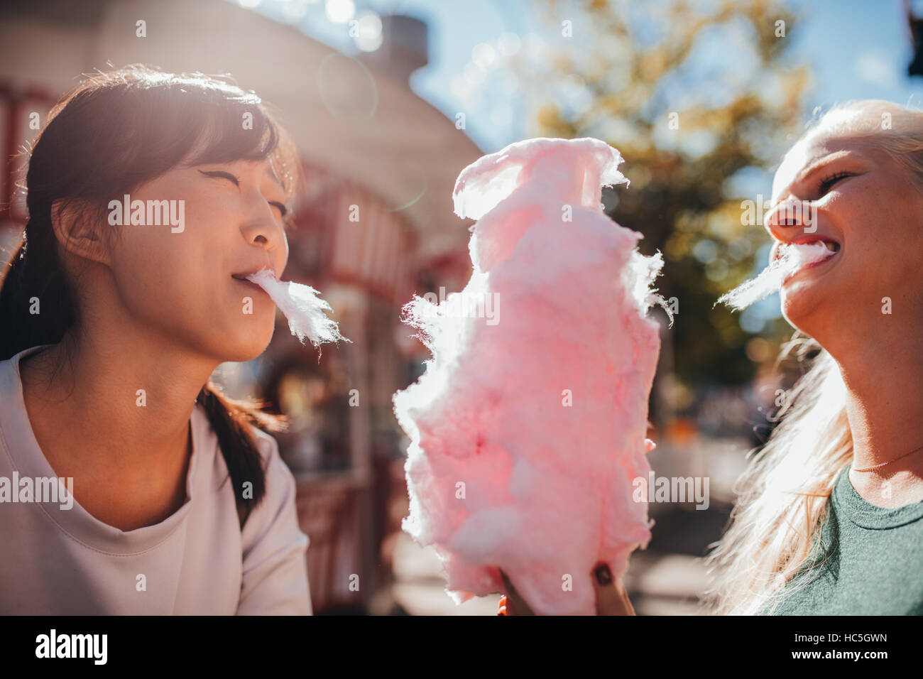 Dos mujeres jóvenes compartiendo el algodón candyfloss en el parque de diversiones. Mejores amigos comer Cotton Candy juntos al aire libre. Foto de stock