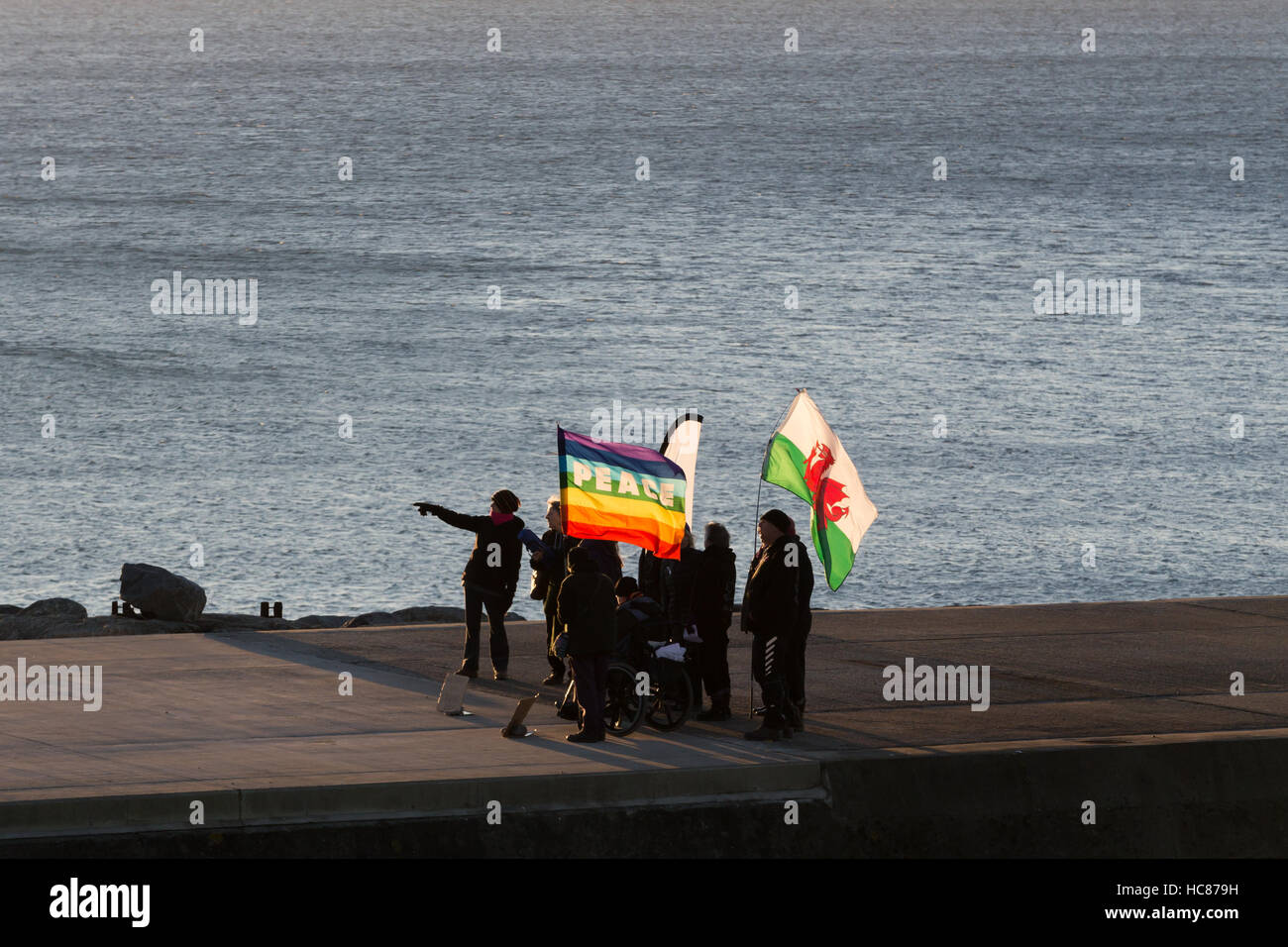 Un grupo de personas de pie en un embarcadero sujetando una bandera de paz y una bandera de Gales Foto de stock