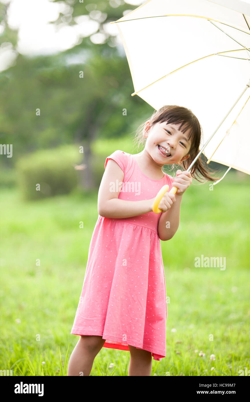 Chica sonriente sosteniendo un paraguas permanente en el campo Foto de stock