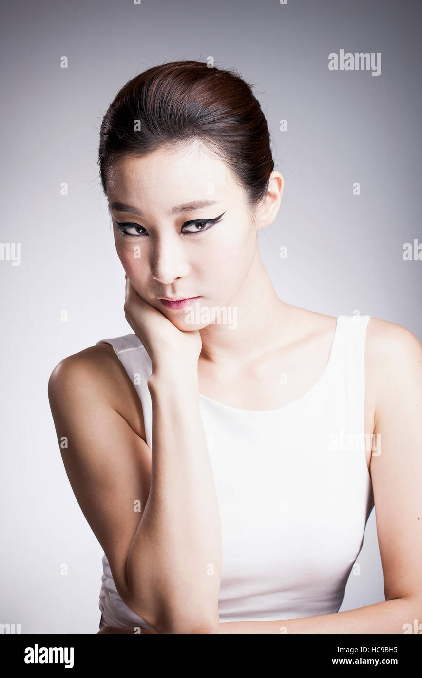 Retrato de joven bella mujer coreana en delineador de ojos negro colocando su barbilla en su mano Foto de stock